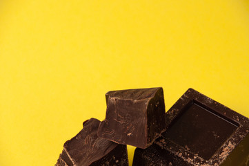 Pieces of black chocolate isolate on a yellow background close-up, copy space from the top