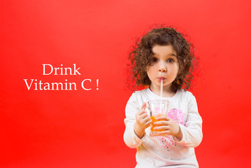 Little girl drinks juice on a red background. Drink Vitamin C