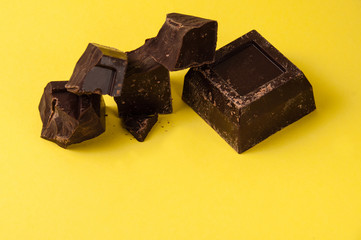 Appetizing pieces of black chocolate isolate on a yellow background close-up, copy space from the bottom