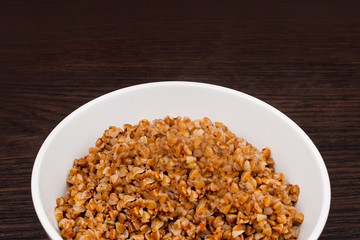 Buckwheat porridge with butter in a small white plate. Buckwheat porridge on a brown background. Bowl with boiled buckwheat. Dietary breakfast. Healthy food