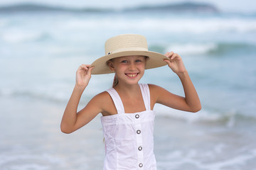 Portrait of a happy Russian little girl in a white dress and hat on a background of the sea. The child walks in the fresh air. Vacation.