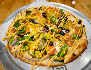 Pizza topped with black olives, jalapeños, spinach, golden corn, pickles, onions, and tomatoes