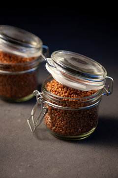 Buckwheat in a glass jar. Buckwheat grain stocks for porridge. Two cans on a table with buckwheat. Food, simple background, still life. Close-up. Place for text.