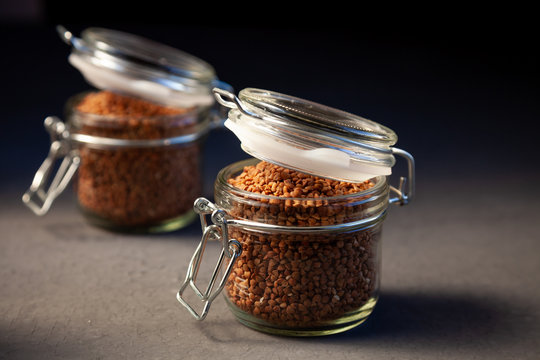 Buckwheat in a glass jar. Buckwheat grain stocks for porridge. Two cans on a table with buckwheat. Food, simple background, still life. Close-up. Place for text.