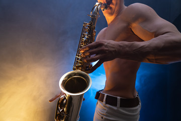 Obraz na płótnie Canvas Muscular man with naked torso playing on saxophone with smoked colorful background 