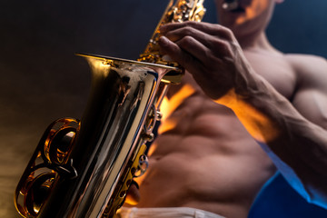 Muscular man with naked torso playing on saxophone with smoked colorful background 