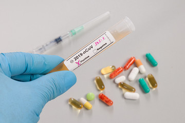 hand in blue gloves holds a test tube after virus analysis with result markers in front of syringe and pills