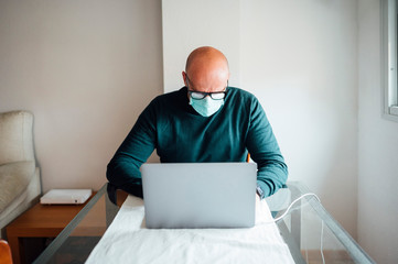 Man working from home on a laptop computer sitting at a desk with mask