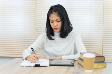 Portrait of a young cheerful Asian female university student studying in self study room in the university library to do her assignment and prepare for examination.