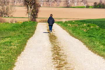 Fototapeta na wymiar Einsamer Junge auf einem Feldweg im Frühling bei Sonnenschein