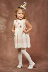 Cheerful little girl with long blond hair in in princess dress and crown