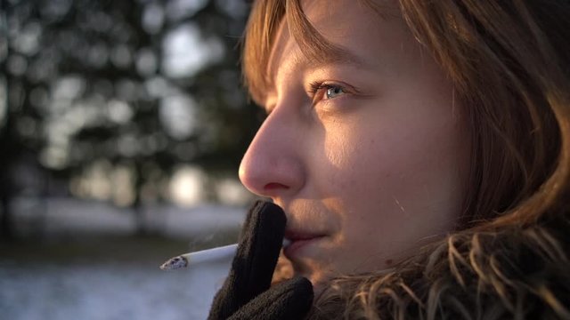 Woman is smoking cigarette in spring city park in slow motion, portrait closeup.