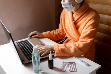 Woman with face mask working in cozy warm bath robe from home office surrounded by sanitizer, nasal...