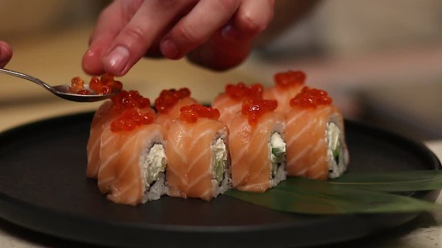  The cook finishes putting red caviar on philadelphia roll.