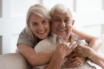 Head shot portrait smiling older wife and husband hugging, looking at camera, family posing for...