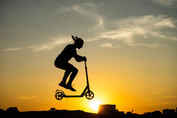 silhouette of a man riding and jumping on kick scooter with beautiful sunrise on background © Hladchenko Viktor