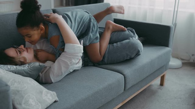 Little young girl playful happy run to mother babysitter nanny lying sofa in cozy apartment daughter like plane jump to mother hug woman loves kissing, concept friendly strong family female happiness