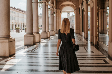 Fototapeta premium A beautiful woman with blond hair walks through the streets of the city. Girl enjoy holidays in Europe. Beautiful historical architecture. Italian weekend. Travel to Turin, Italy. Adventure lifestyle