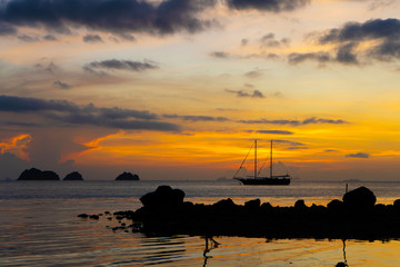 Colorful sunset on a tropical beach. Orange sunset on the ocean. Colorful sunset in the tropics. In the water is a sailing ship. Silhouetted sailboat with masts