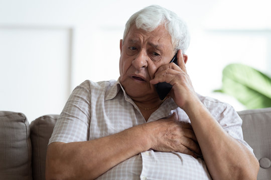 Upset older man touching chest, calling emergency, talking on phone, unhappy mature male having heart attack, lonely grandfather suffering from heartache disease at home, feeling pain, sitting alone