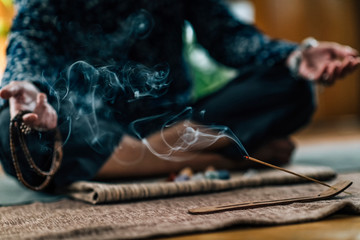 Fototapeta premium Mindful Woman Meditating with Burning Incense Sticks, Sitting in Lotus Pose. Hands in Lap, Palms Facing Upwards