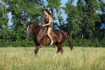 Naklejka na ściany i meble Beautiful girl riding on a horse bareback in evening summer fields