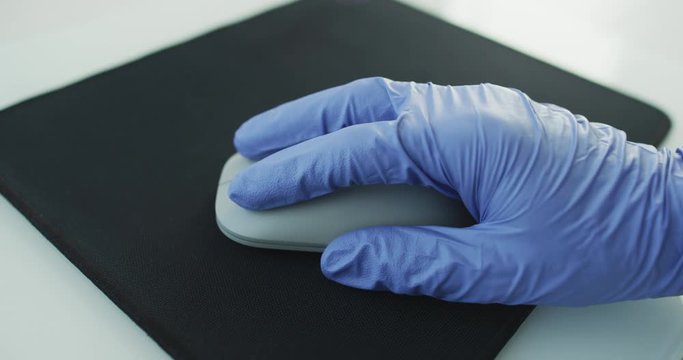Doctor or nurse or office worker using protective gloves while using computer mouse working at PC at hospital or work in order to stop spreading of coronavirus, COVID-19.