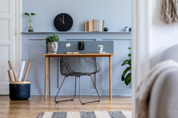 Scandinavian home office interior with wooden desk, design chair, wood panleing with shelf, plant, black clock, office supplies and elegant accessories in modern home decor.