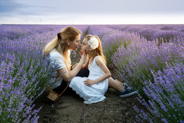 Mother and little daughter sit and enjoy between rows of blooming lavender field at golden hour...