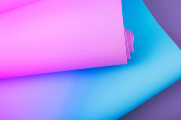 Top view of neon colored blue pink yoga mat on violet background. Space for text.