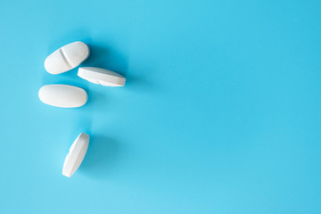 White pills on blue background with copy space, top view. Painkiller or antibiotic. Healthcare and...