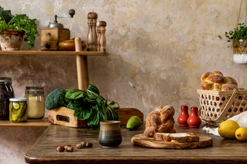 Stylish composition of kitchen interior with family table, vegetables, tea pot, dessert, shelf with food supplies, plants, herbs and kitchen accessories in wabi sabi concept of home decor. 