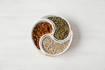 Peeled sunflower seeds, pumpkin seeds and raisins lie on a white table in a beautiful round plate divided into compartments, top view. Organic, vegetarian products that increase the body 's immunity