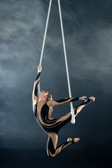 A young girl performs the acrobatic elements in the air trapeze. Studio shooting performances on a...