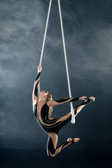 A young girl performs the acrobatic elements in the air trapeze. Studio shooting performances on a black background