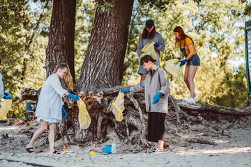 Group of activists friends collecting plastic waste on the beach. Environmental conservation.