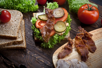 sandwich with smoked meat, green salad, fresh tomatoes and pickled cucumbers, on kitchen wooden table background