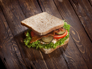 sandwich with smoked meat, green salad, fresh tomatoes and pickled cucumbers, on kitchen wooden table background