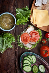 turkey meat sandwich with tomatoes, cheese, green salad and cucumbers on dark wooden table background