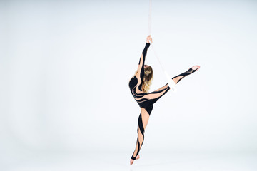 Young woman gymnast wearing black costume on trapeze on white background