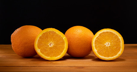 Fresh and juicy half and slice of orange fruit on a wooden table and black background.