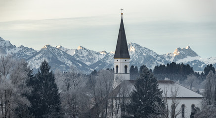 Aerial view of the small cozy german town at the mountain bottom at sunrise in a winter season, Halblech city, Germany, Bavaria, Branches of trees are covered with hoarfrost, sunny weather