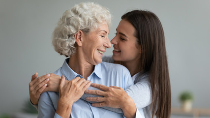 Happy mature mom and grown-up daughter hug and cuddle look in eyes enjoy tender moment together,...
