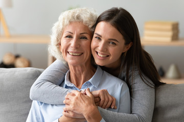 Portrait of happy elderly mom and grown-up daughter hug embrace posing together relaxing on couch...