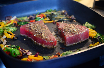 Cooking fresh tuna steaks on skillet. Sautéing vegetables. Preparing and cooking colorful food. Beautiful food preparation, chef cooking gourmet meal.