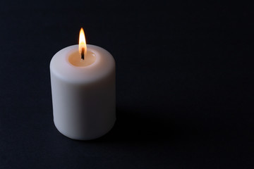 Fototapeta na wymiar a thick white candle lit with an orange-red flame burning on a black background