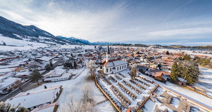 Aerial view of the small cozy german town at the mountain bottom at sunrise in a winter season, Halblech city, Germany, Bavaria, Branches of trees are covered with hoarfrost, sunny weather