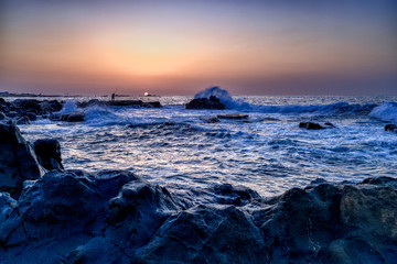 朝日に照らされる岩場の釣り人