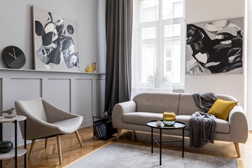 Modern scandinavian home interior of living room with design gray sofa, armchair, marble stool, black coffee table, stylish paintings, decoration and elegant personal accessories in home decor.