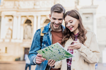 Selective focus of couple looking at map and smiling in city